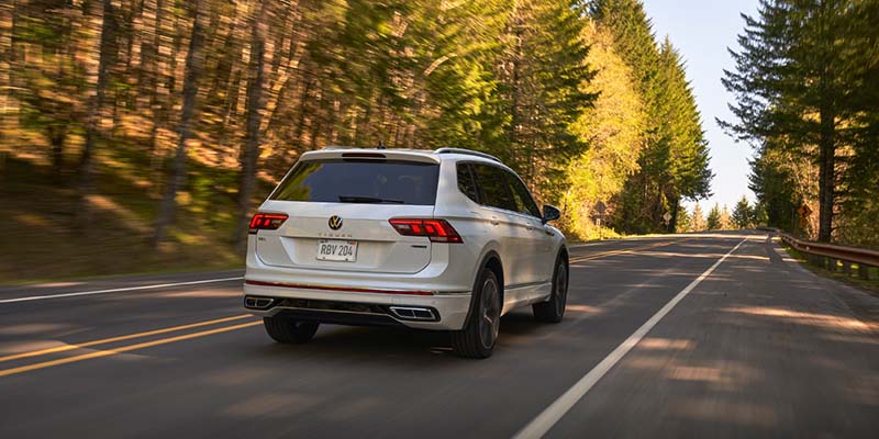 White Volkswagen Tiguan driving down a road surrounded by trees.