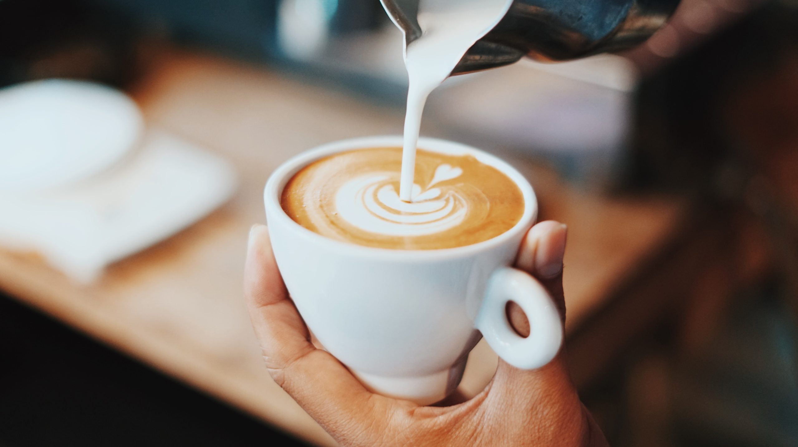 A person pouring milk into a latte.